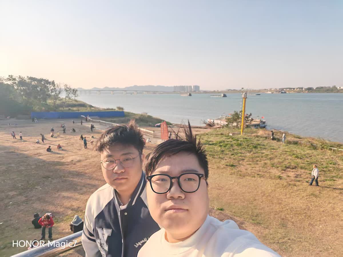 江边草坡上与朋友的自拍，远处是大桥和灯塔